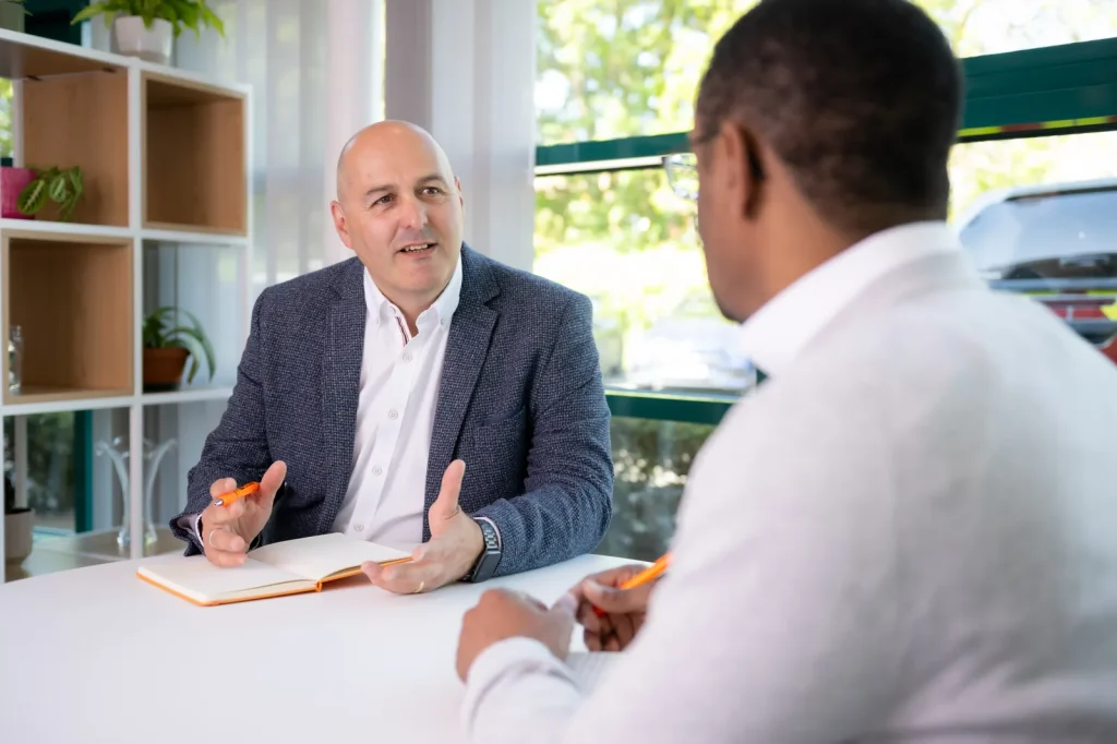 Colin Tapscott in a blazer coaching a client across a table, explaining a point with his hands
