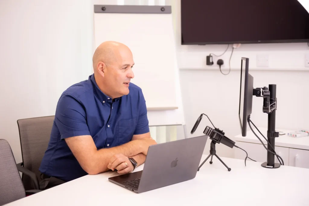 Colin Tapscott recording at a desk with a laptop and microphone in an Everyday Leader podcast setup