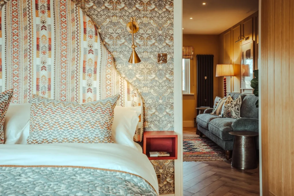 Bedroom styled by Wildkind Interiors with a patterned headboard, William Morris wallpaper and a view through to a cosy sitting room