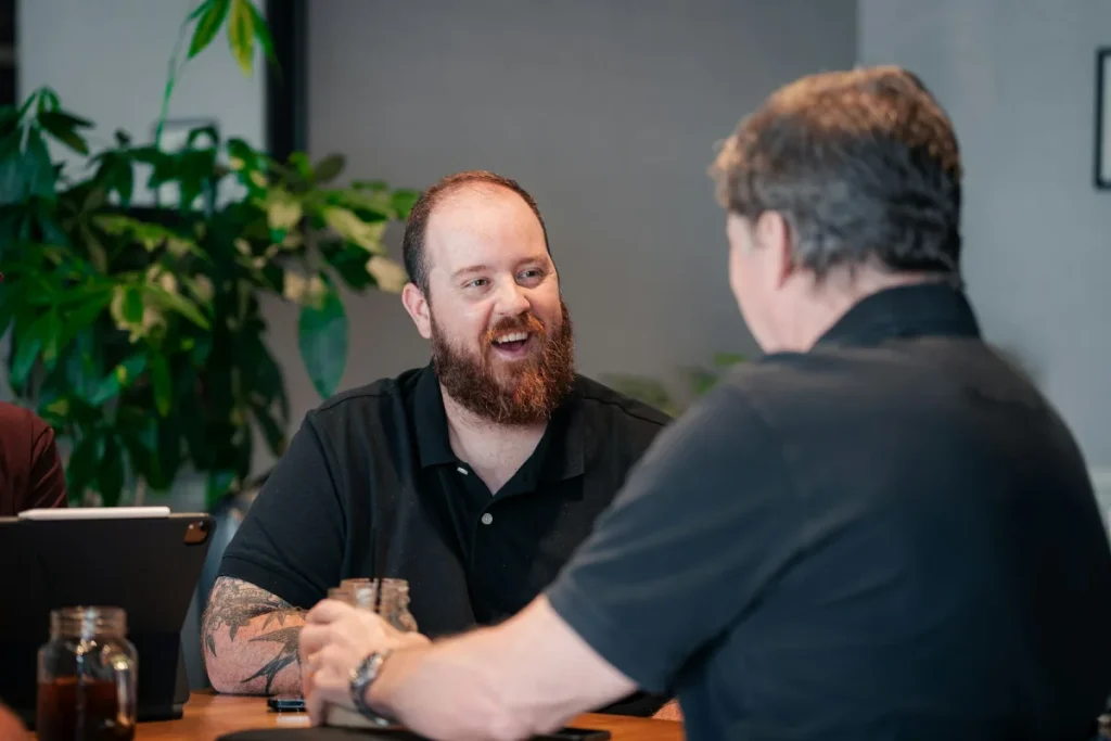 Two people in conversation across a table, the working relationship Higher Performance builds with clients